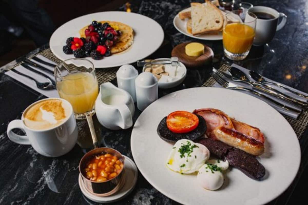A breakfast setting with plates of eggs, bacon, tomatoes, and beans, accompanied by coffee and juice.