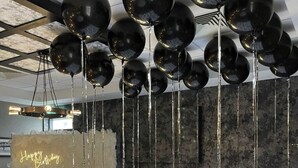 Een kamer met een donkere, structuurrijke muur, een groot verlicht getal '18' en zwarte ballonnen die aan het plafond hangen.