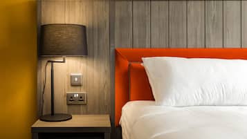 Une chambre d’hôtel avec une tête de lit en bois, une table de chevet avec une lampe et une prise électrique.