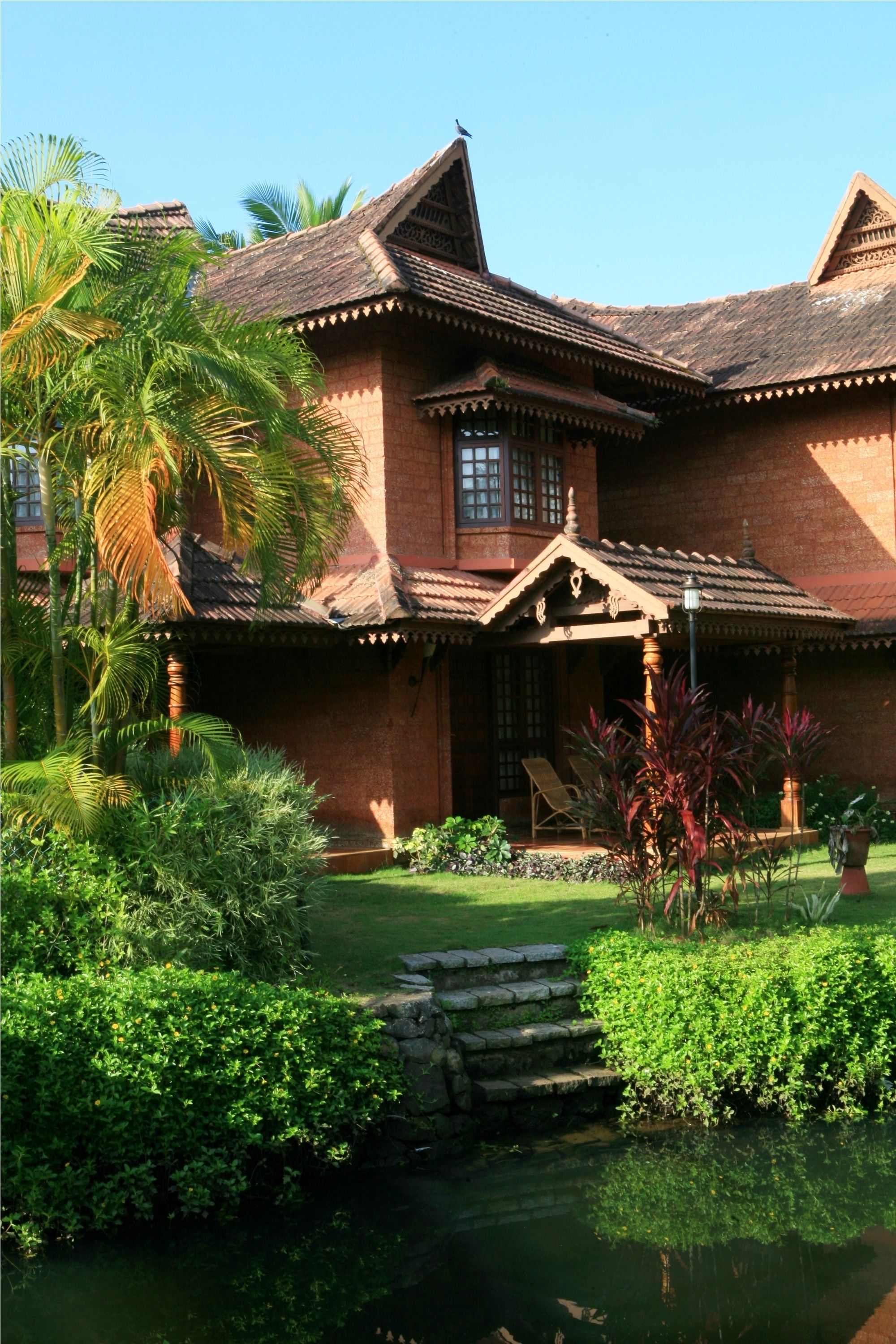 A traditional house with a tiled roof, a porch with a chair, and a small pond in the garden.