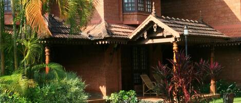 A traditional house with a tiled roof, a porch with a chair, and a small pond in the garden.