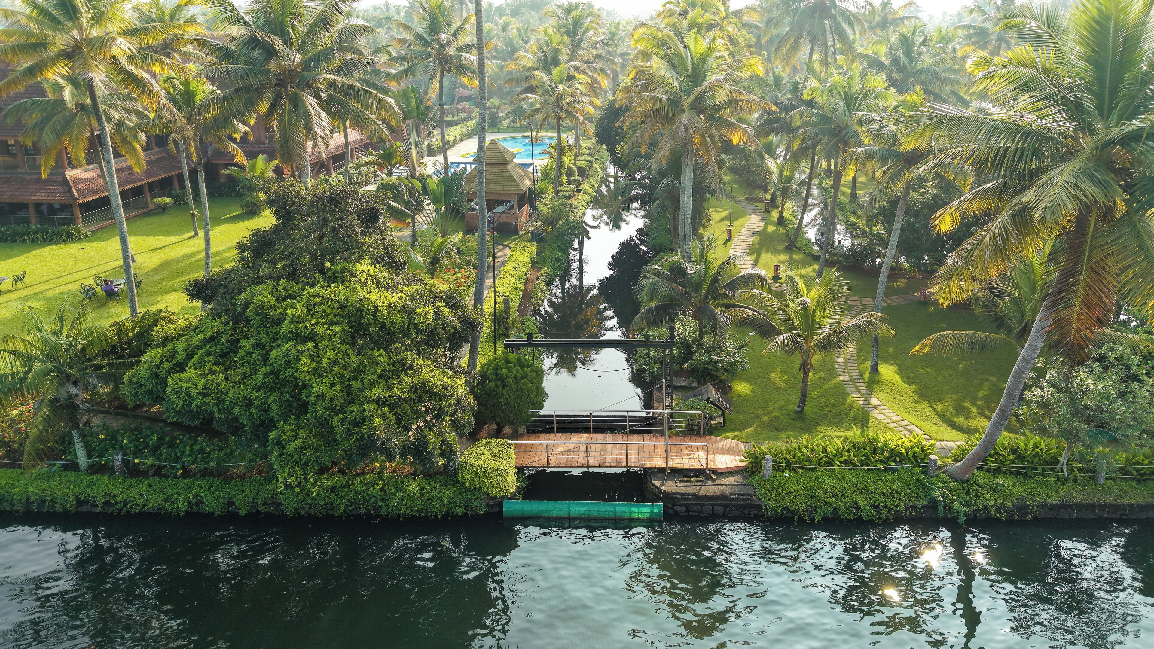 A tropical resort with a water body, palm trees, and a pathway.