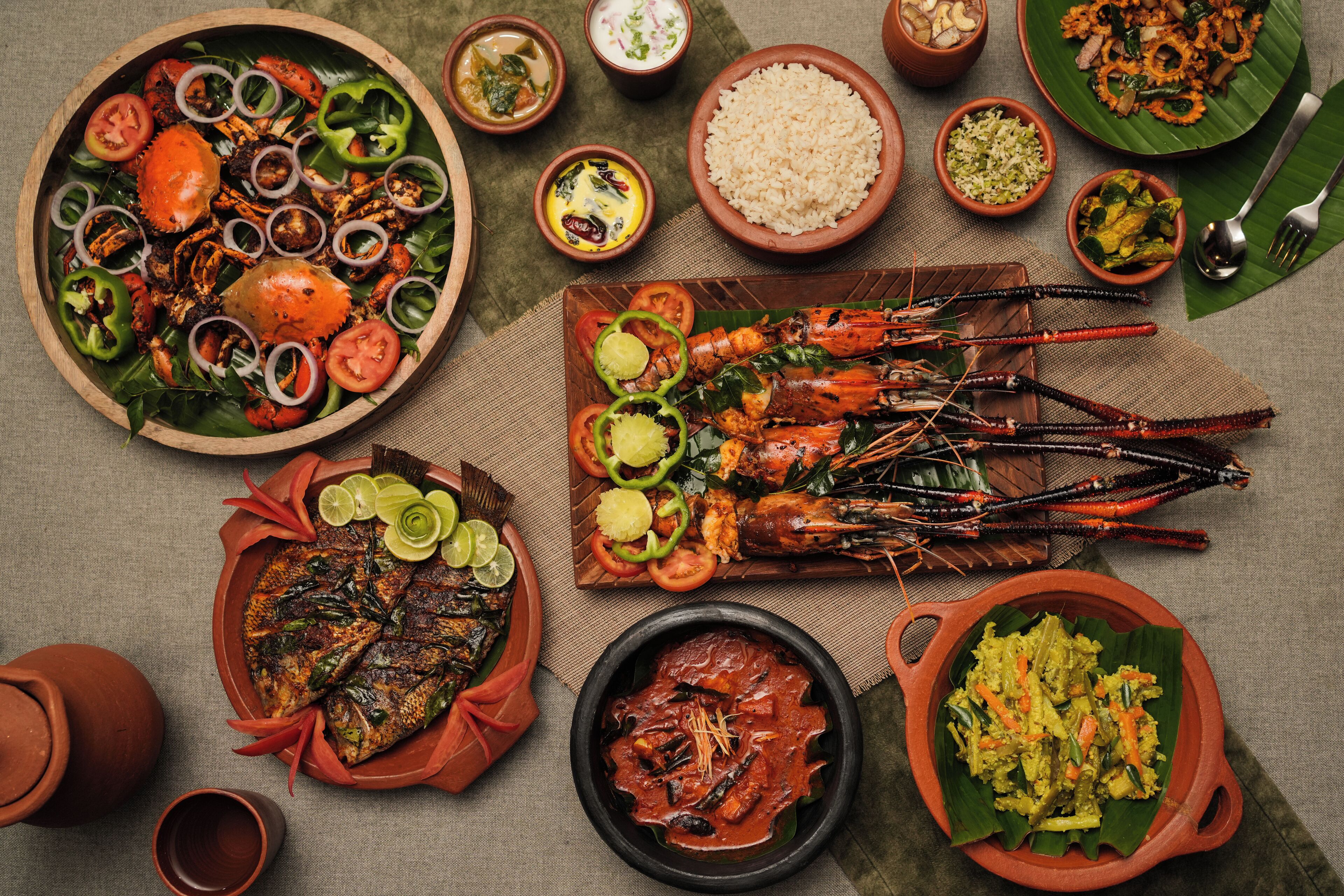 Verschiedene Meeresfrüchtegerichte, darunter gegrillter Fisch und Garnelen, serviert auf traditionellen Tonplatten und Bananenblättern.