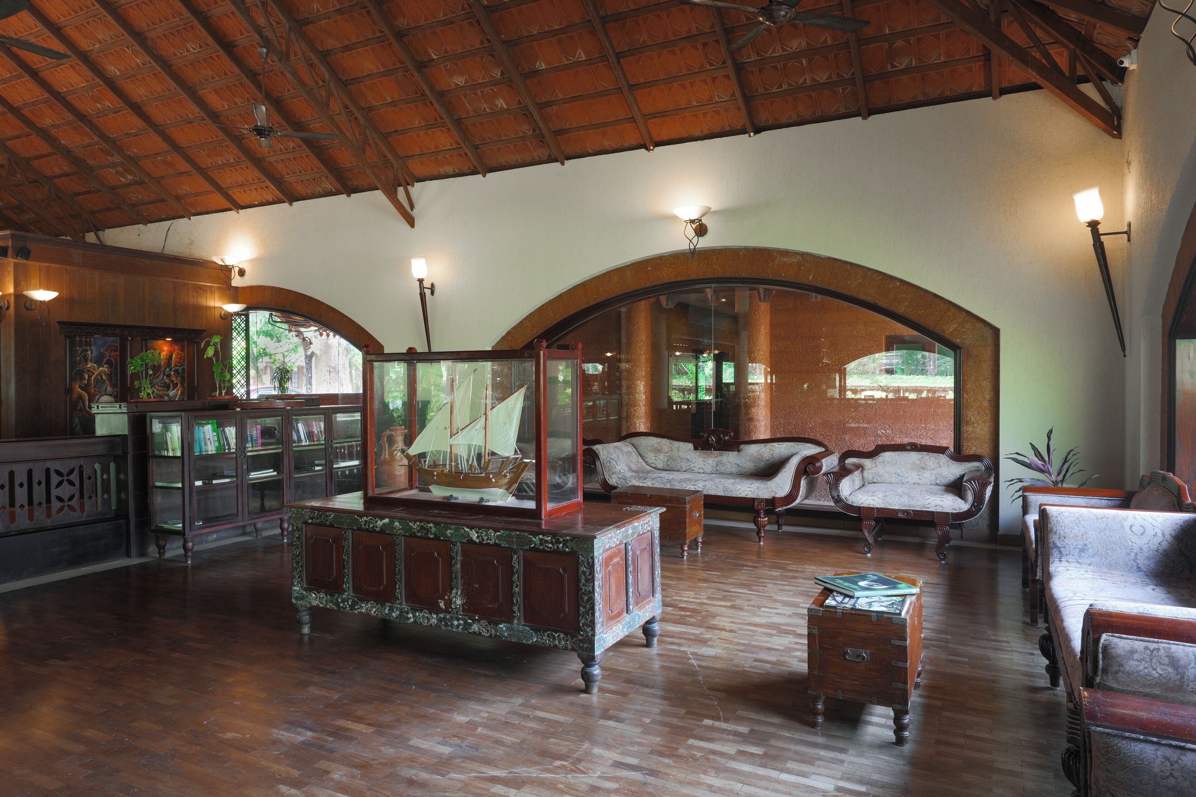 A spacious room with wooden flooring, a high ceiling, and arched windows. There are several pieces of furniture including a sofa, chairs, and a cabinet.