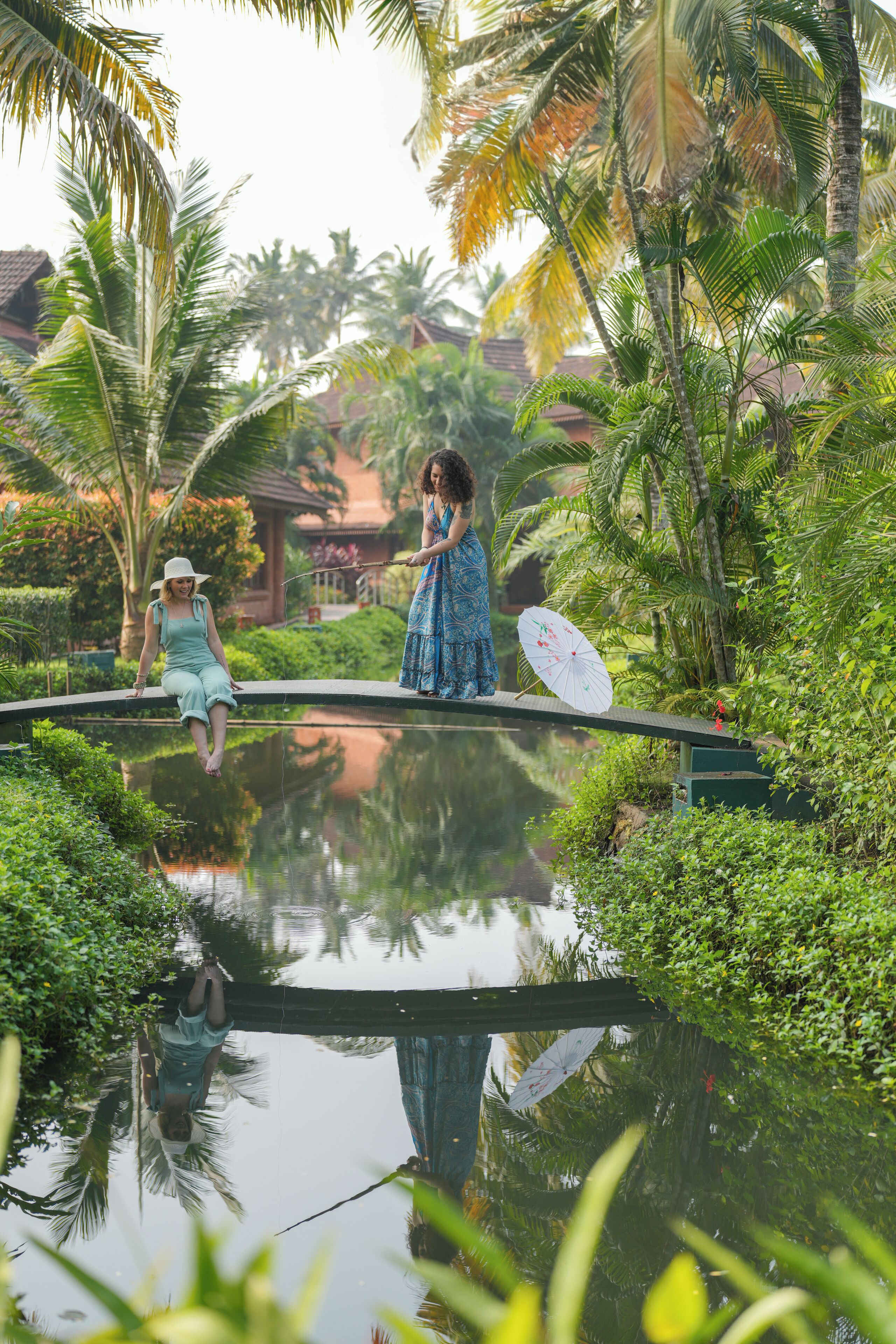 A bridge over a reflective water body with lush greenery and palm trees.
