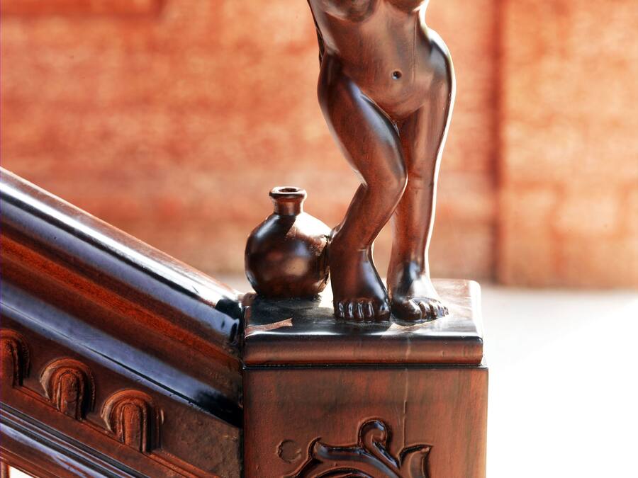 Una estatua de bronce de un querubín sobre una barandilla de madera, con un muro de ladrillo al fondo.