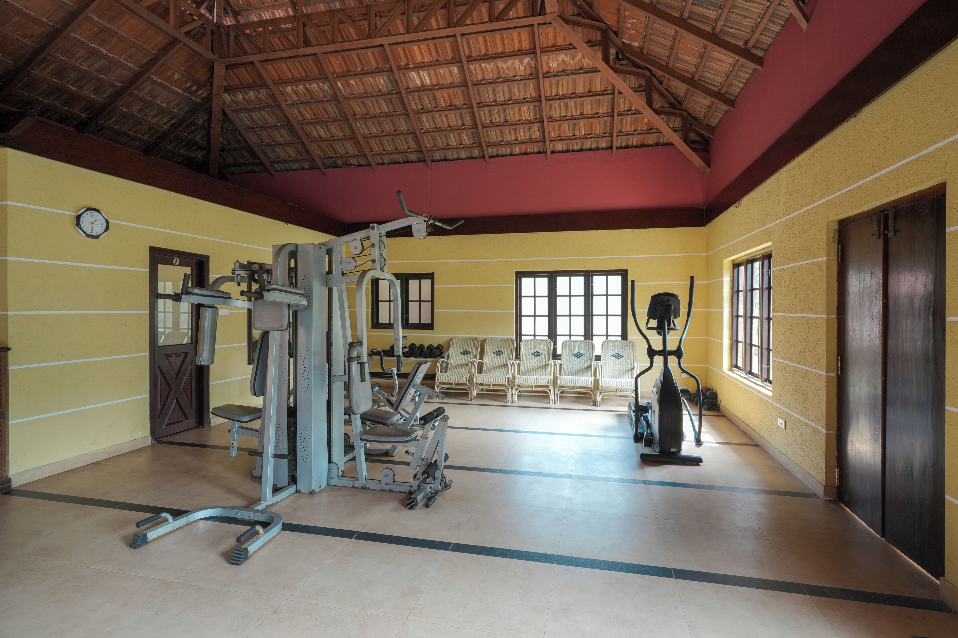 A gym with exercise equipment, a clock, and windows.