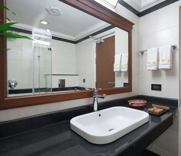A modern bathroom with a large mirror, a white sink, and a black countertop. - Lakesong Kumarakom (Kottayam)