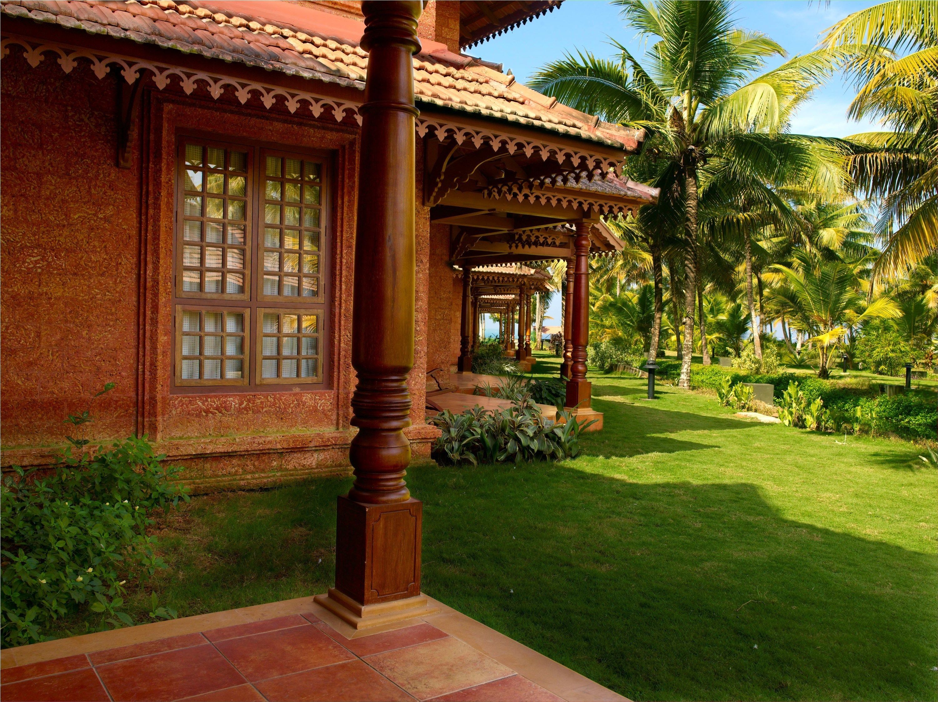 A traditional building with a tiled roof, a wooden column, and a well-maintained garden with palm trees and grass.