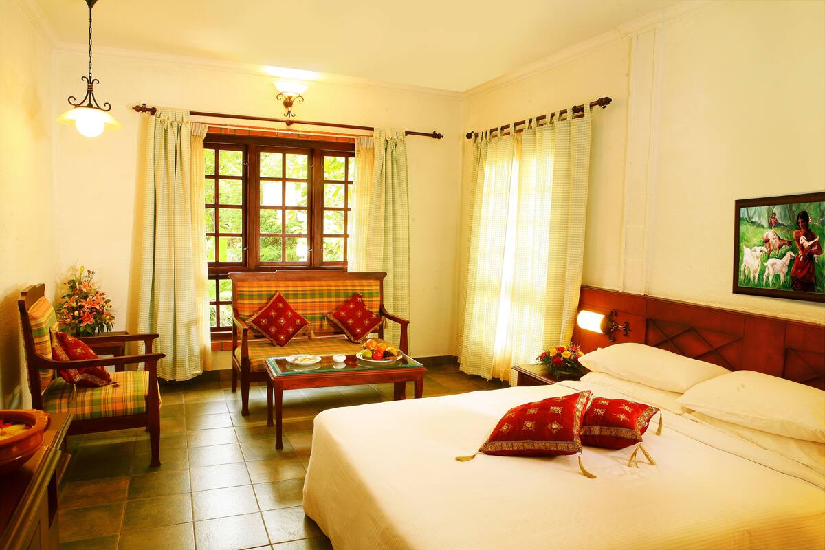 A hotel room with a bed, a table with a vase of flowers, a chair, and a window with curtains.