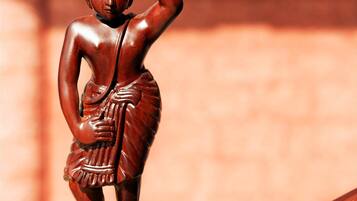 Una estatua de madera de una figura que lleva un objeto grande en la cabeza, sobre un pedestal de madera.