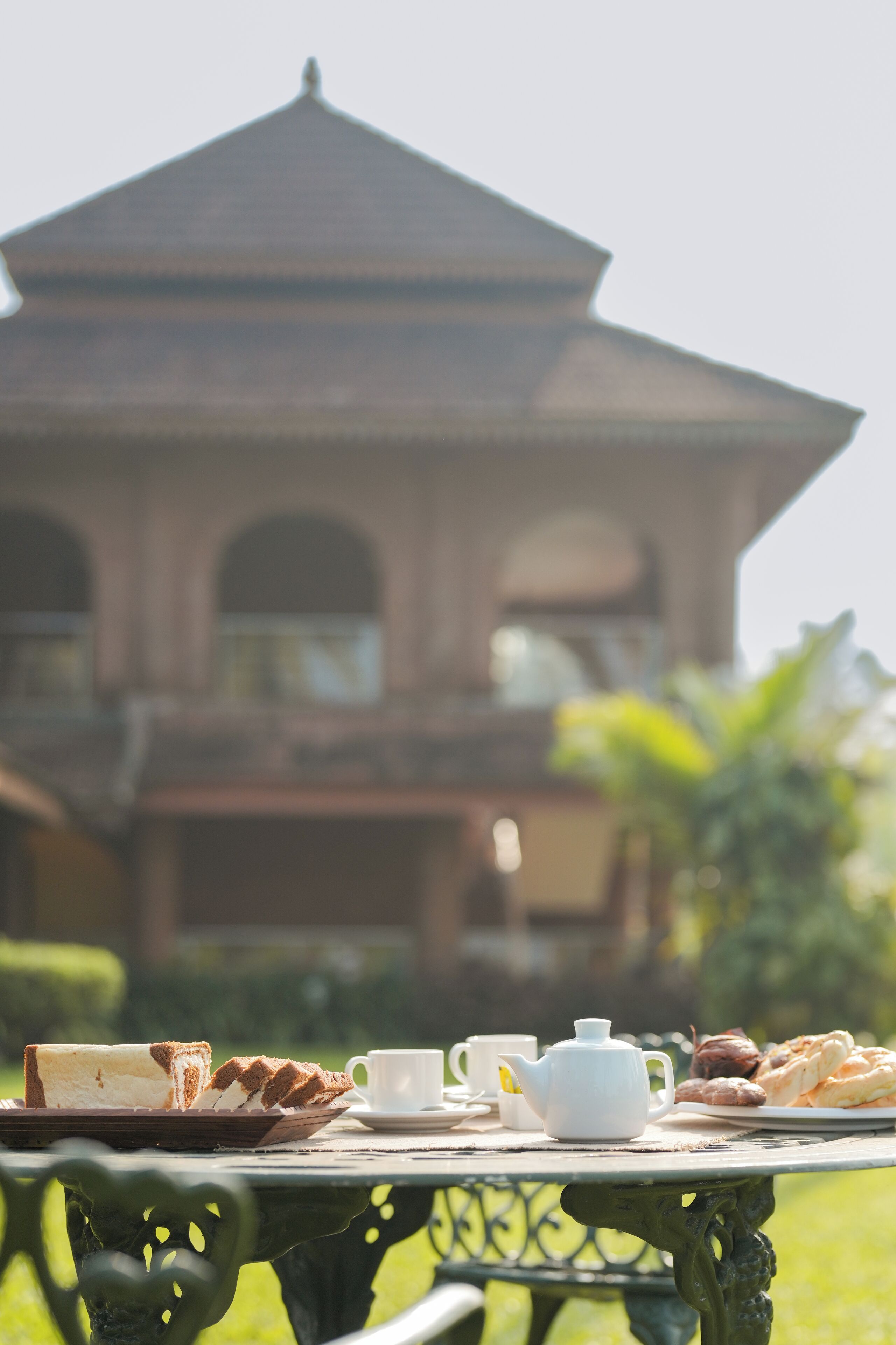 A table set with a teapot, cups, and pastries in an outdoor setting with a building in the background.