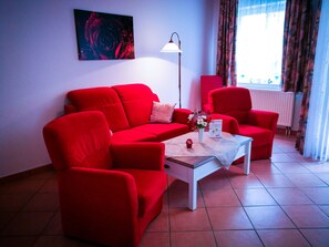 A red sofa, a white coffee table, a red armchair, a floor lamp, and a painting on the wall.