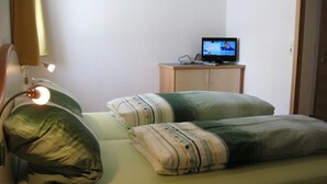 Makuuhuone, jossa on sänky, tyynyjä, televisio, joka on sijoitettu kaappiin, ja lamppu.