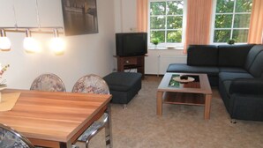 Ein Wohnzimmer mit einer Couch, einem Couchtisch, einer TV-Konsole und einem Essbereich mit Stühlen und einem Tisch.