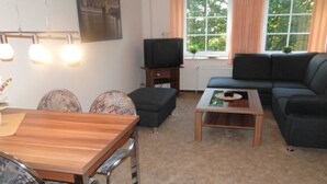 Ein Wohnzimmer mit einer Couch, einem Couchtisch, einem Fernseher und einem Esstisch mit Stühlen.