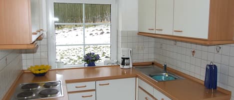 Eine Küche mit weißen Schränken, einem Herd, einer Spüle und einem Fenster mit Blick auf eine verschneite Landschaft.