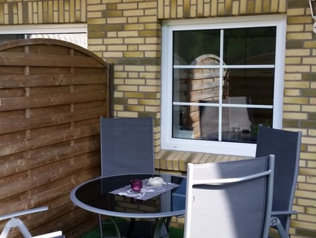 Un espace patio avec une table ronde et deux chaises, un portail en bois et une fenêtre donnant sur un tonneau.