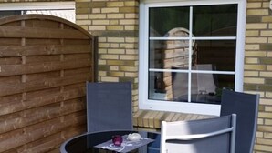 Eine Terrasse mit einem runden Tisch und zwei Stühlen, einem hölzernen Tor und einem Fenster mit Blick auf ein Fass.