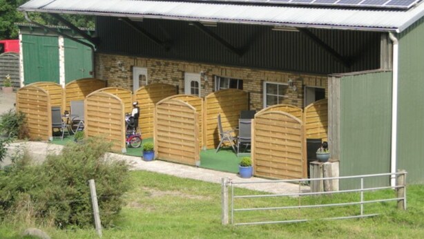 Ein Gebäude mit einer Solaranlage auf dem Dach, Holzkonstruktionen und einem eingezäunten Bereich.