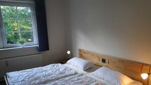 Ein Schlafzimmer mit einem hölzernen Kopfteil, einem großen Bett mit weißer Bettwäsche, einem Fenster mit Blick auf Grünflächen und Nachttischlampen.
