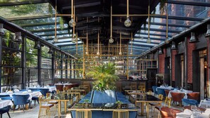 A restaurant with a glass ceiling, tables with blue tablecloths, and hanging light fixtures.