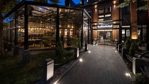 A glass-enclosed restaurant with outdoor seating, a brick building with an 'Industrial' sign, and a paved walkway.