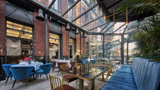 A restaurant with a glass ceiling, blue chairs, and a long blue sofa.