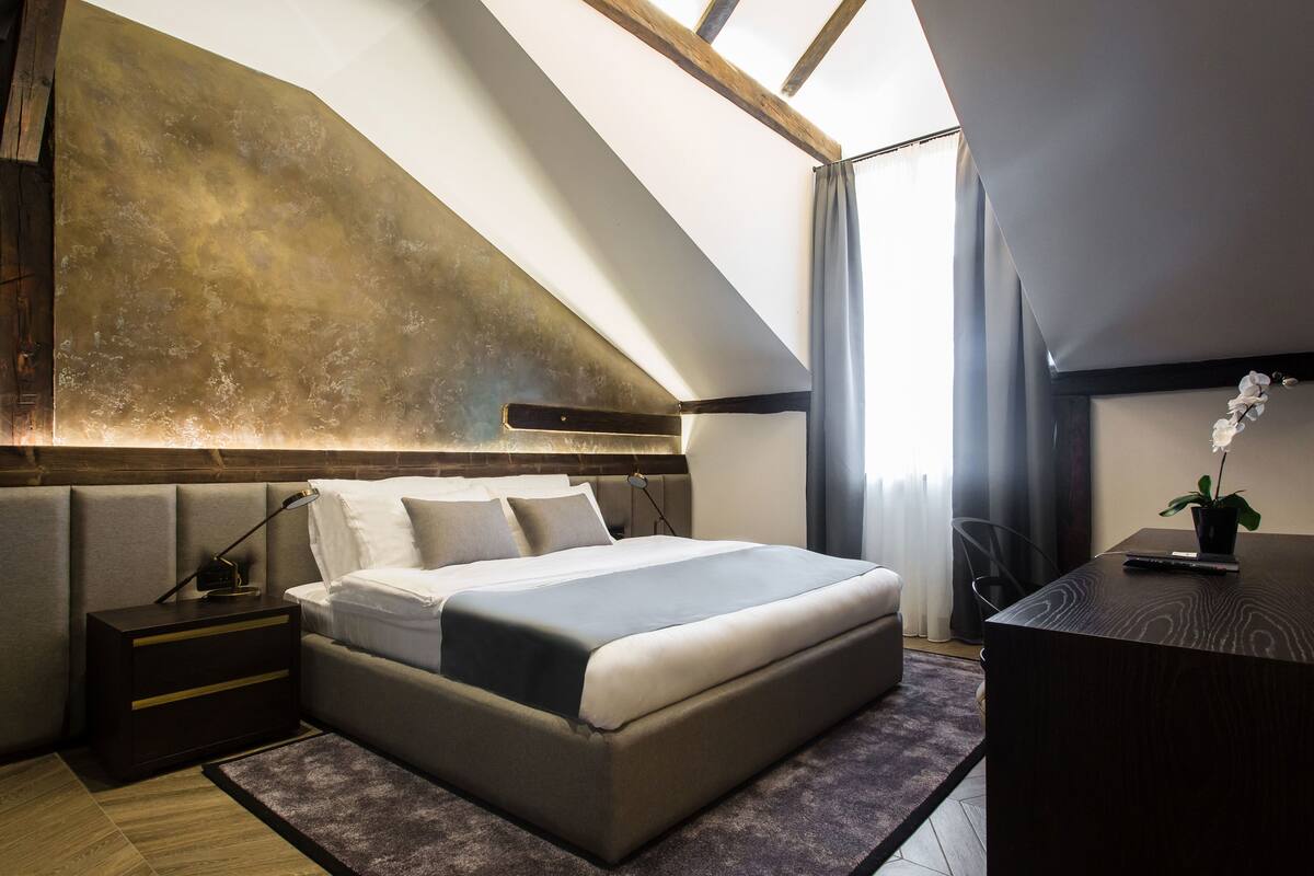 A modern bedroom with a large bed, a nightstand, a desk, and a skylight.