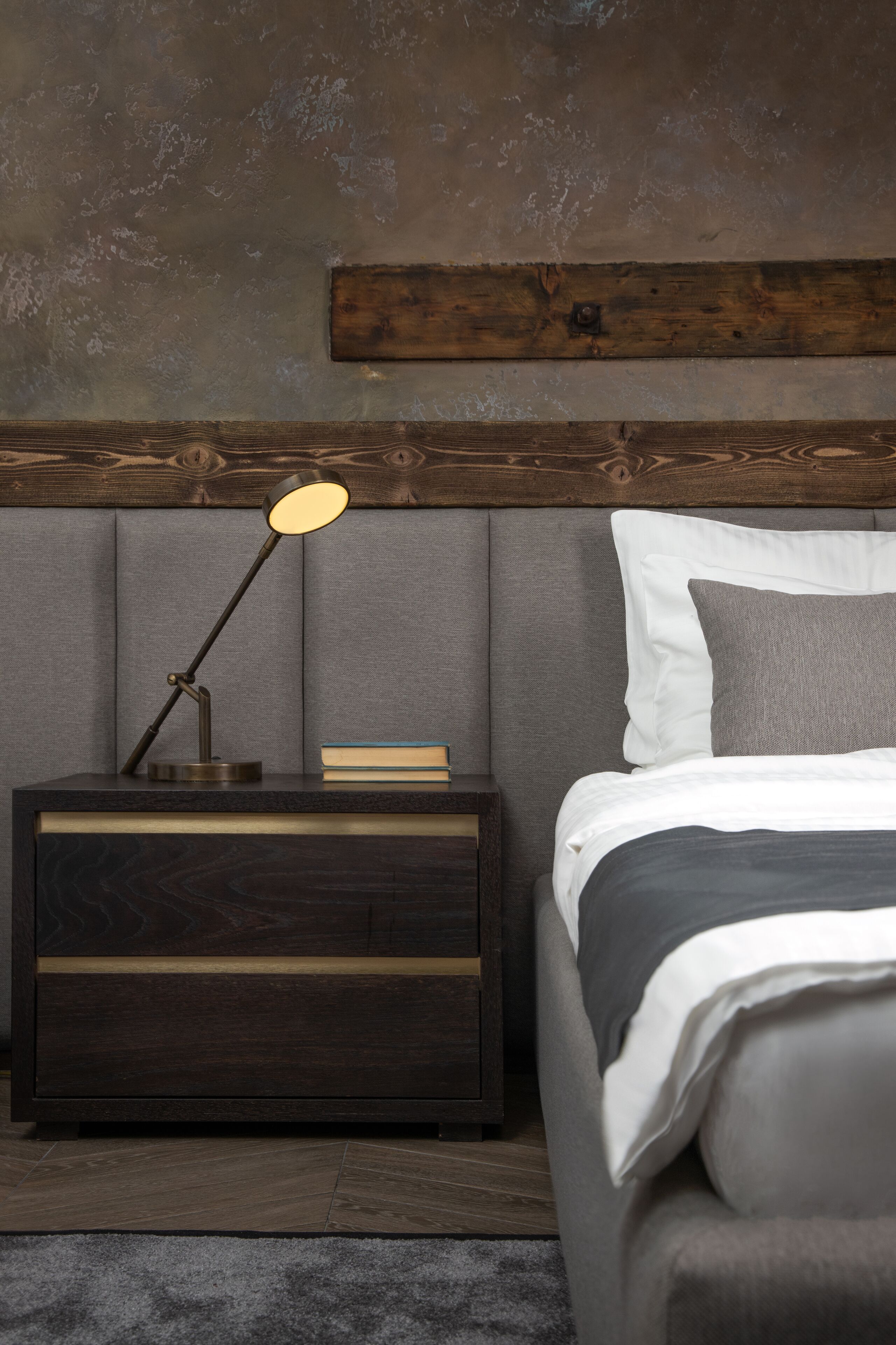 A bedroom with a wooden headboard, a bedside table with a lamp, a bed with pillows, and a book on the table.