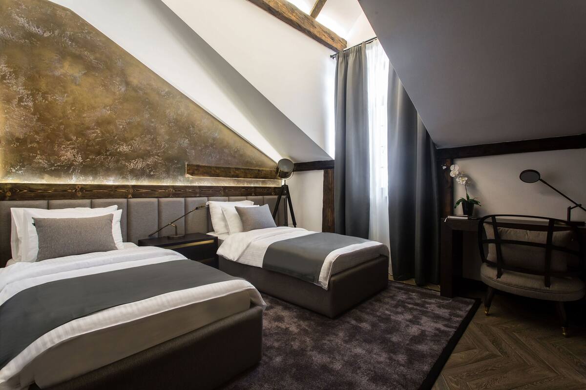 A bedroom with two beds, a desk, a chair, and a large window with curtains.