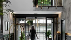 A modern lobby with a double door entrance, a metal staircase, and a large potted plant.