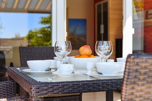 A dining table set with white tableware and fruit, with wicker chairs and a view of the outdoors. - Vacation apartment 7 - Haus Südermole (Esens)