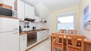 Una cucina moderna con mobili bianchi, un forno a microonde, un piano cottura e un'area pranzo con sedie e tavolo in legno.