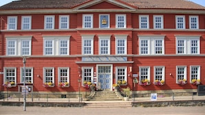 Un bâtiment rouge avec une entrée centrale, de nombreuses fenêtres et des jardinières.