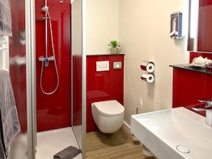 Ein modernes Badezimmer mit rotem und weißem Farbdesign, inklusive einer Duschkabine, einer weißen Toilette und einem weißen Waschbecken mit Spiegel darüber.