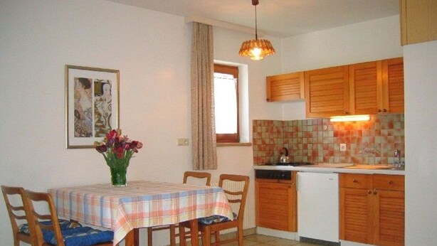 A dining area with a table and chairs, a kitchen with wooden cabinets, and a hanging light fixture.