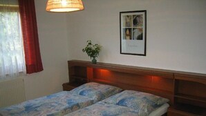 A double bed with patterned bedding, a bedside table, a wall-mounted picture, and a window with curtains.