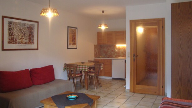 Una sala de estar con sofá, una mesa de centro, una zona de comedor con sillas, una cocina con armarios y una puerta.
