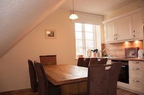A kitchen with a wooden table, chairs, a hanging light, and white cabinets.