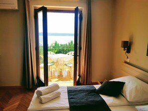 A hotel room with a bed, a view of a balcony with outdoor furniture, and a wall-mounted lamp. - Family Apartment Kocevar (Piran)