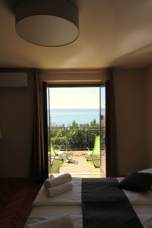 A hotel room with a bed, a view of the sea, and a balcony with chairs.