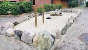 Zona de juegos arenosa con rocas grandes y un conjunto de columpios de madera.