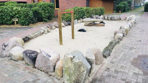 Zona de juegos arenosa con rocas grandes y un conjunto de columpios de madera.