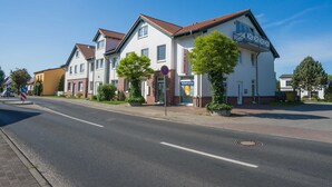 A row of white residential buildings with red-tiled roofs, a clear sky, and a street in front. - An der Pappelwende - five-room apartment type H5 (Karlshagen)