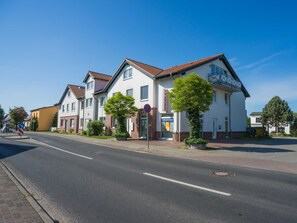 A row of white residential buildings with red-tiled roofs, a clear sky, and a street in front.