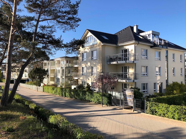 A multi-story residential building with balconies, a paved driveway, and surrounding greenery.