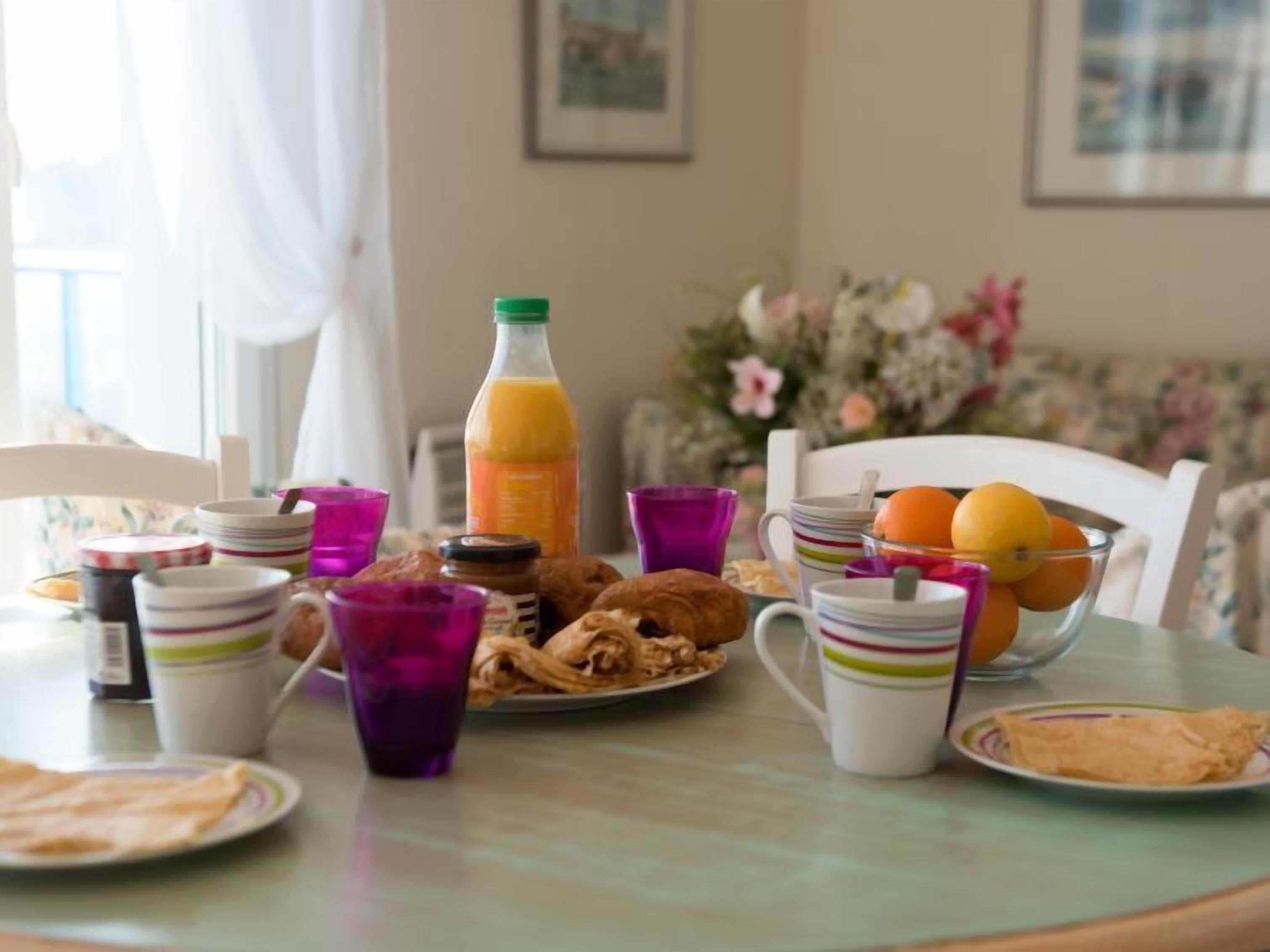 Une table de petit-déjeuner avec divers aliments, notamment des croissants, du jus d’orange et un bol d’oranges.