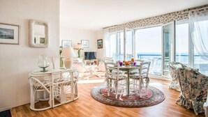 A spacious living area with a round table, white chairs, a large window with a view, and a patterned rug. - Apartment Hoédic by Interhome (Quiberon)