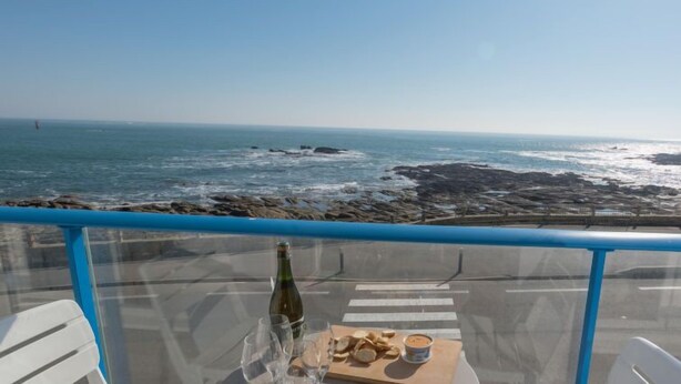 A table with a bottle and glasses, a wooden board with snacks, and a view of the ocean and rocky shore. - Apartment Hoédic by Interhome (Quiberon)